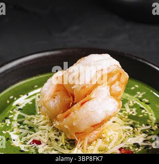 Nourriture, présentation gourmande de soupe de crevettes aux épinards ornée de garnitures dans un bol sombre sur une surface texturée Banque D'Images