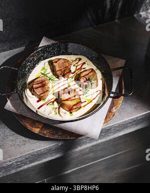 Food, Un plat gastronomique avec de tendres morceaux de viande disposés magnifiquement dans un bol sombre. Le repas comprend des sauces arrosées et des herbes fraîches, serties sur un woo Banque D'Images