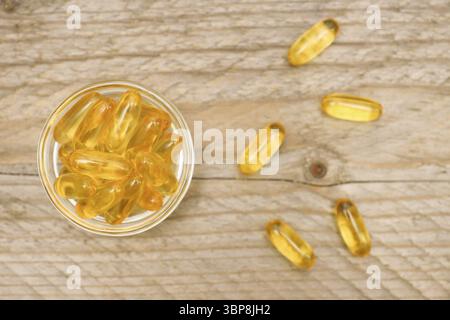 Bol en verre avec capsules d'huile de poisson sur fond en bois, vue de dessus Banque D'Images