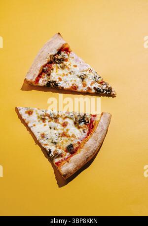 Nourriture, deux tranches de pizza sont placées sur une surface jaune vif, présentant du fromage fondu, des garnitures riches et une croûte dorée. Les couleurs créent un chee Banque D'Images