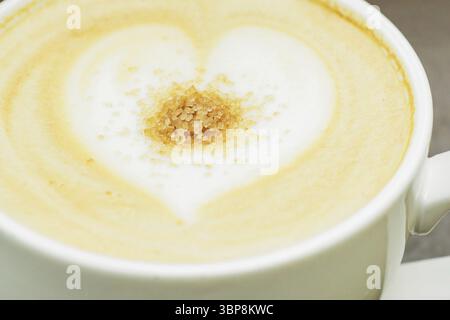 Gros plan d'une grande tasse de cappuccino fraîchement préparé avec de la mousse douce et de la cassonade et dessiner le cœur par le barista Banque D'Images