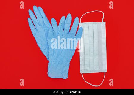 Paire de gants médicaux bleus en latex et masque contour d'oreille chirurgical sur fond rouge. Concept de coronavirus de protection Banque D'Images
