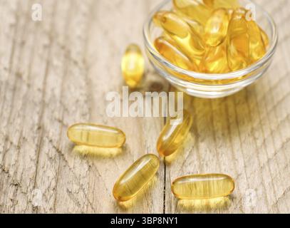 Gélules d'huile de foie de poisson oméga 3 dans un petit bol en verre. Gros plan de pilules translucides dorées. Complément nutritionnel en acides gras sains Banque D'Images
