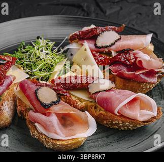Nourriture, Une assiette magnifiquement présentée de pain grillé garnie de diverses charcuteries, fromage et tomates séchées. Les légumes verts frais complètent la saveur savoureuse Banque D'Images
