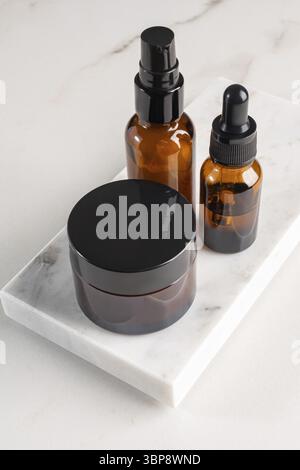 Trois maquettes de produits cosmétiques sur podiums de marbre. Contexte pour la présentation de cosmétique. Flacons en verre ambré avec couvercles noirs Banque D'Images