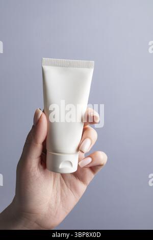 Main tenant le tube en plastique blanc vierge sur fond gris. Maquette de marque de produit de beauté cosmétique. Soins de la peau Banque D'Images