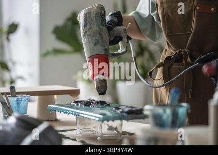 Artiste féminine utilisant le séchoir pour disperser la résine époxy sur la peinture, créer le dessin des vagues de la mer sur la toile. Une femme ingénieuse et créative manipule habilement t Banque D'Images