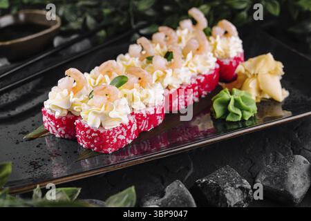 Nourriture, rouleaux de sushi exquis nappés de crevettes, de caviar et de sauce crémeuse sur une assiette noire élégante Banque D'Images