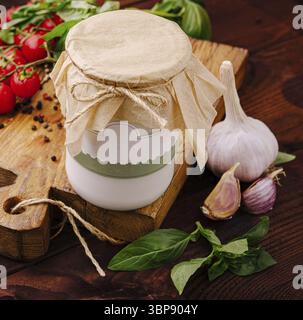 Nourriture, Une table en bois rustique affiche un pot de sauce à l'ail, entouré de basilic frais, de gousses d'ail et de tomates cerises mûres. Le réglage évoque un W. Banque D'Images