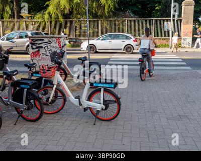 Bologne, Italie le 3 juillet 2025 Une femme roule sur un vélo électrique de partage RideMovi, traversant un passage piétonnier à Bologne, en Italie, tandis que d'autres électri Banque D'Images
