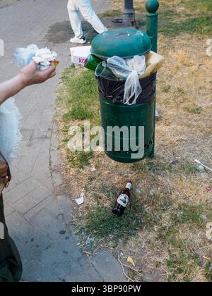 Bologne, Italie 3 juillet 2025 piéton passant le bac à ordures public trop rempli dans la rue urbaine, révélant les défis de la gestion des déchets pendant les périodes de pointe Banque D'Images