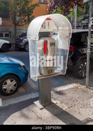 Bologne, Italie 3 juillet 2025 cabine téléphonique publique avec combiné rouge debout sur un trottoir à Bologne, Italie, avec des voitures garées et des arbres dans le dos Banque D'Images