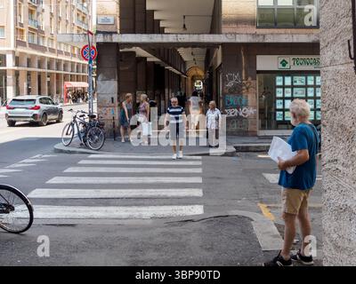Bologne, Italie 3 juillet 2025 homme senior debout sur la rue étroite de Bologne, lisant le journal, observant les piétons passant alors que les vélos vintage le Banque D'Images