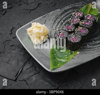 Nourriture, Une assiette de rouleaux de sushi au sésame noir repose élégamment sur une surface texturée. Les rouleaux sont garnis de thon rose et servis avec du gingembre mariné Banque D'Images