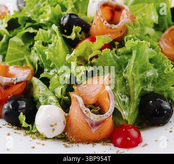 Nourriture, salade de saumon fraîche et saine avec laitue verte, olives noires, tomates cerises et fromage mozzarella servis sur assiette blanche Banque D'Images
