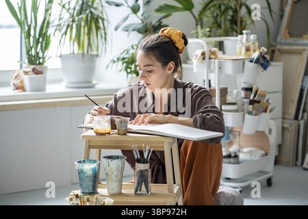 Peinture d'artiste féminine concentrée à l'aquarelle. Fille inspirée focalisée engagée dans un passe-temps créatif, processus de travail au home studio. Femme fabriquant du ske Banque D'Images