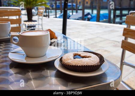 Deux tasses fraîches de cappuccino dans des tasses en céramique blanche servies avec une pâtisserie fourrée au chocolat surmontée d'un motif de coeur, placées sur une table métallique dans un Banque D'Images