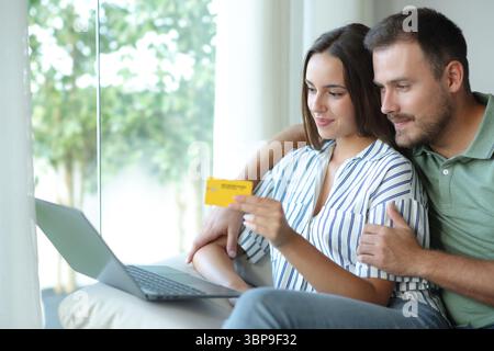 Couple satisfait payant en ligne avec carte de crédit et ordinateur portable assis dans un canapé à la maison Banque D'Images