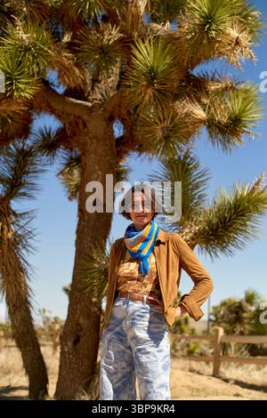 Personne en vêtements décontractés se tient devant un grand arbre dans un paysage désertique ensoleillé. Désert de Mojave, États-Unis Banque D'Images
