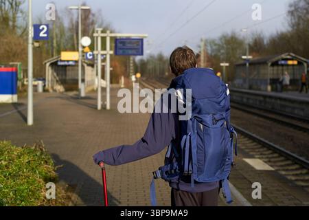 Voyageur avec sac à dos et bâton de marche attend seul sur une plate-forme de gare déserte. Weser Uplands, Allemagne Banque D'Images