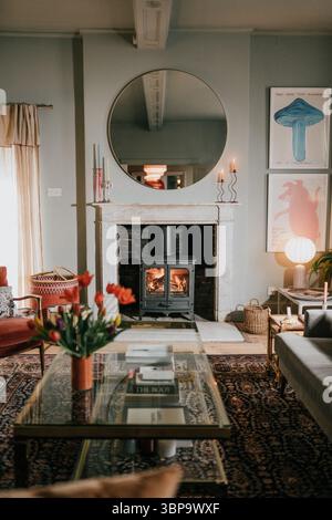 Un salon avec une cheminée et un miroir rond. La chambre est décorée avec quelques œuvres d'art, dont une peinture d'un champignon. La chambre dispose d'un Banque D'Images