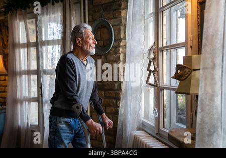 Vieil homme avec une béquille se sentant déçu, perdu dans des pensées tristes seul à la maison. Veuve homme mûr. Banque D'Images