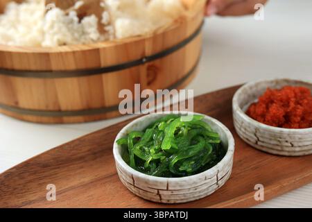 Salade d'algues wakame avec graines de sésame et piment dans un petit bol sur une assiette en bois Banque D'Images
