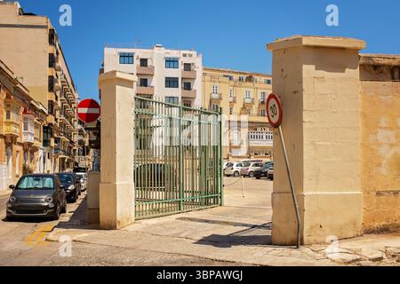 Ruelle urbaine avec limitation de vitesse et panneaux d'interdiction d'entrée à l'entrée d'une aire de stationnement avec portes métalliques, bâtiments résidentiels et voitures garées à l'arrière Banque D'Images