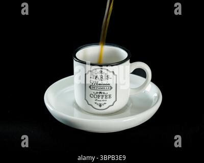 Café foncé versé dans une tasse en céramique blanche avec un design vintage Paris, placé sur une soucoupe assortie sur un fond de tissu noir. Parfait. Banque D'Images