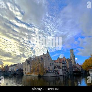 Canal pittoresque à Bruges, Belgique avec la tour du beffroi au loin sous un paysage nuageux spectaculaire. Banque D'Images
