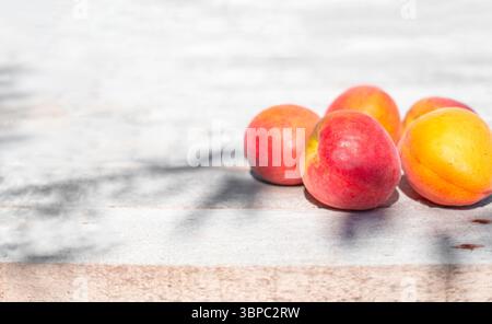 Les abricots mûrs colorés reposent sur une surface en bois ensoleillée. Récolte des fruits. Banque D'Images