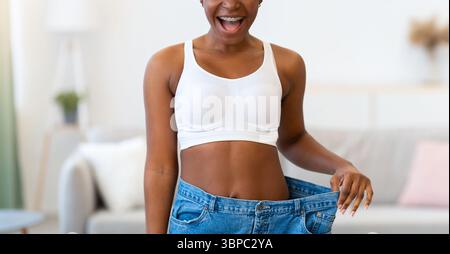 Femme noire heureuse portant Big Jeans après perte de poids à la maison Banque D'Images