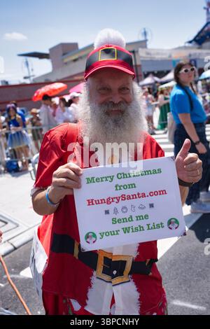 Un homme habillé en Père Noël, avec une longue barbe blanche, tient un panneau publicitaire HungrySanta.com et demande des listes de souhaits. Il porte une chemise rouge et Banque D'Images