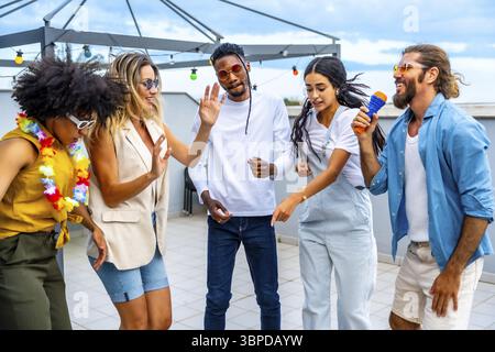 Groupe d'amis joyeux multi-ethniques s'amusant à chanter karaoké et danser ensemble lors d'une fête sur le toit Banque D'Images