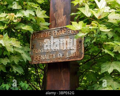 Vieux signe de propriété privée rouillé sur un poteau en bois entouré de feuillage, Bugbrooke village, Northamptonshire, Royaume-Uni Banque D'Images