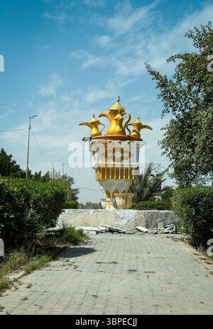 Un monument doré saisissant se dresse en Irak, flanqué d'une végétation luxuriante sous un ciel bleu clair, mettant en valeur l'art local. Banque D'Images