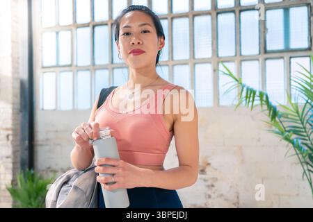 Confiante jeune femme habillée en vêtements athlétiques tenant une bouteille d'eau prête pour un mode de vie actif Banque D'Images