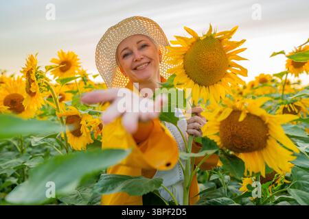 Une femme joyeuse souriante debout parmi un grand champ de tournesol portant un chapeau élégant Banque D'Images