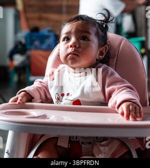 Une petite fille est assise dans une chaise haute à la maison en Indonésie, mettant en valeur la vie de famille quotidienne. Banque D'Images