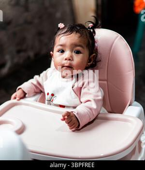 Une petite fille est assise dans une chaise haute à la maison en Indonésie, mettant en valeur la vie de famille quotidienne. Banque D'Images