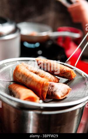 Rouleaux de printemps dorés croustillants égouttant l'huile sur une passoire en métal dans un cadre de cuisine maison. Parfait pour les thèmes culinaires, asiatiques ou culinaires. Banque D'Images