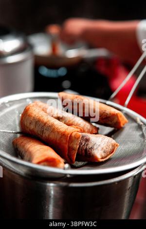 Rouleaux de printemps dorés croustillants égouttant l'huile sur une passoire en métal dans un cadre de cuisine maison. Parfait pour les thèmes culinaires, asiatiques ou culinaires. Banque D'Images