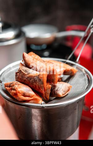 Rouleaux de printemps dorés croustillants égouttant l'huile sur une passoire en métal dans un cadre de cuisine maison. Parfait pour les thèmes culinaires, asiatiques ou culinaires. Banque D'Images