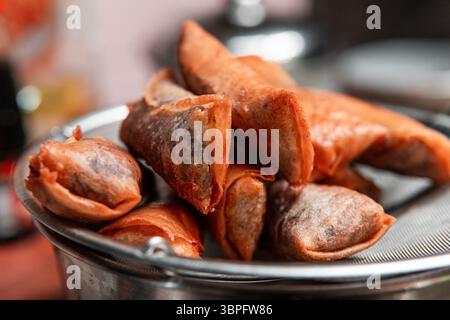Rouleaux de printemps dorés croustillants égouttant l'huile sur une passoire en métal dans un cadre de cuisine maison. Parfait pour les thèmes culinaires, asiatiques ou culinaires. Banque D'Images