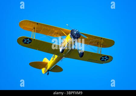 Un biplan Boeing Stearman jaune vif volant dans le ciel bleu. Californie, États-Unis. Banque D'Images