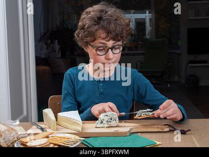 Pays-Bas, Boy étale des fromages français sur des craquelins. Devant lui se trouve le fromage bleu ou fromage bleu, qui est un fromage fait avec des cultures de t Banque D'Images