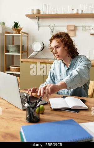 Beau jeune homme s'engage activement à étudier dans un bureau à domicile moderne rempli de lumière naturelle. Banque D'Images