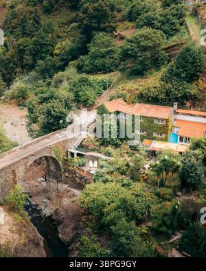 Vue aérienne du vieux pont de pierre menant au bâtiment couvert de lierre niché au milieu du feuillage verdoyant, Ribeiro Frio, Madère, Portugal. Banque D'Images