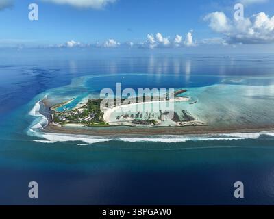 Vue aérienne de la verdure luxuriante d'une station balnéaire rencontrant le lagon bleu et les poulets spot de surf par une journée calme où les nuages se reflètent dans la mer plate, Thulusdhoo, Banque D'Images