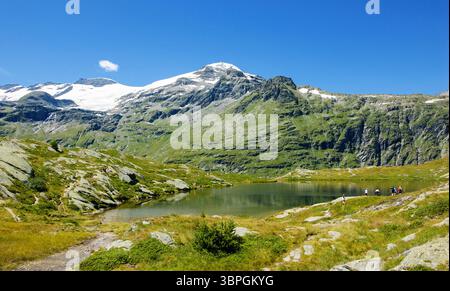Les randonneurs se reposent au petit lac de montagne avec une vue magnifique sur les sommets enneigés du parc national de la Vanoise dans les Alpes françaises. (Savoie, France). Banque D'Images